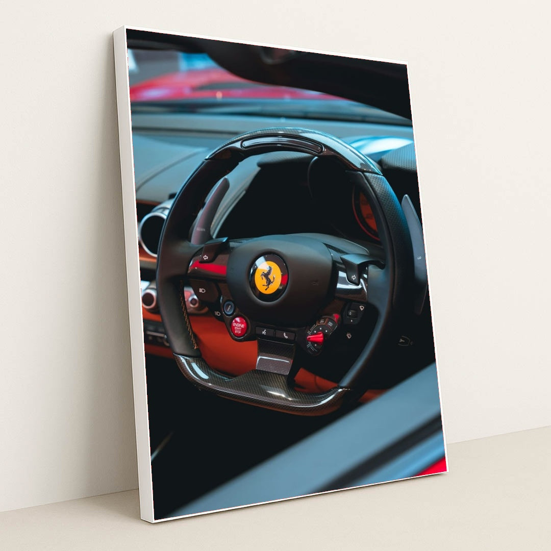 This photo shows the black carbon fiber steering wheel of a Ferrari, with red accents and dashboard controls, in a white frame.