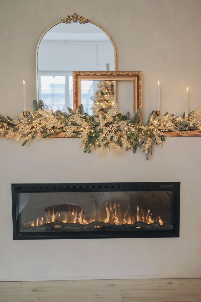 Valeria Boltneva - A beautifully decorated fireplace for Christmas with candles, greenery, and a festive reflection in mirrors.