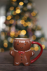 Valeria Boltneva - Cute gingerbread man mug in front of a blurred Christmas tree with lights.