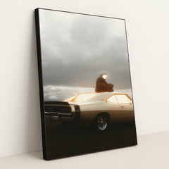 This photo shows a person in an astronaut suit sitting on the roof of a classic Dodge Charger at dusk, in a black frame.