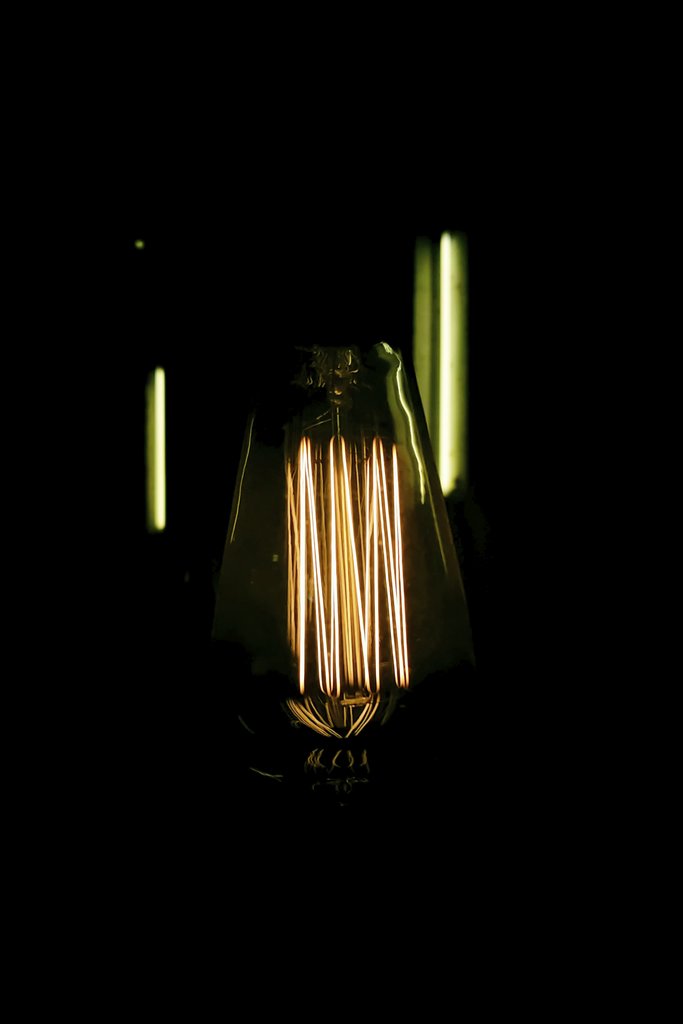 Allec Gomes - Close-up of a glowing vintage Edison light bulb with a dark background and visible filament.