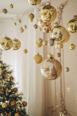 Valeria Boltneva - Elegant golden Christmas ornaments hanging in a festive living room with a tree.
