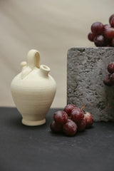 Cup of  Couple - A minimalist still life featuring a ceramic vase alongside fresh grapes on a textured backdrop.