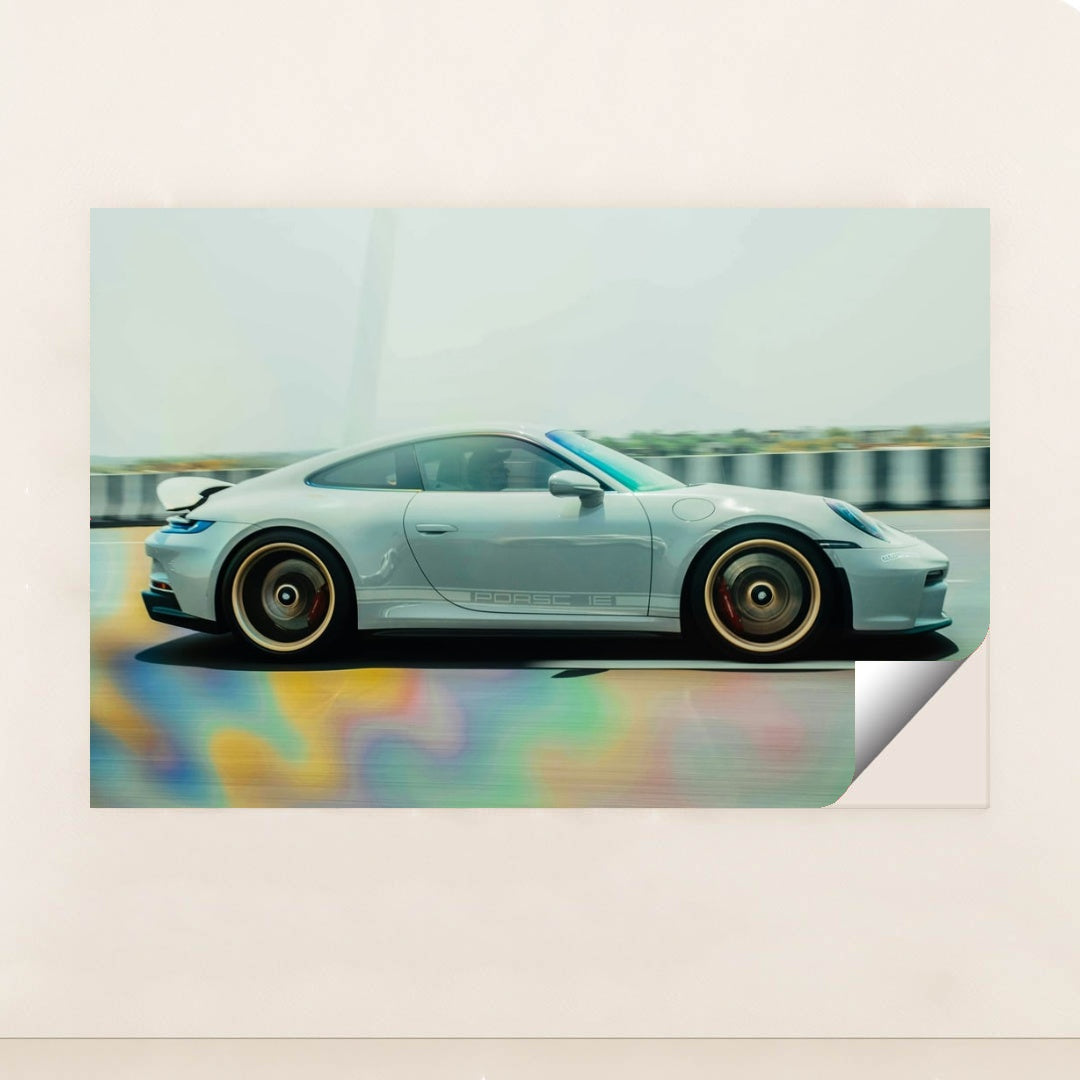 This photo shows a silver Porsche sports car in motion on a highway with colorful reflections on the road, unframed.