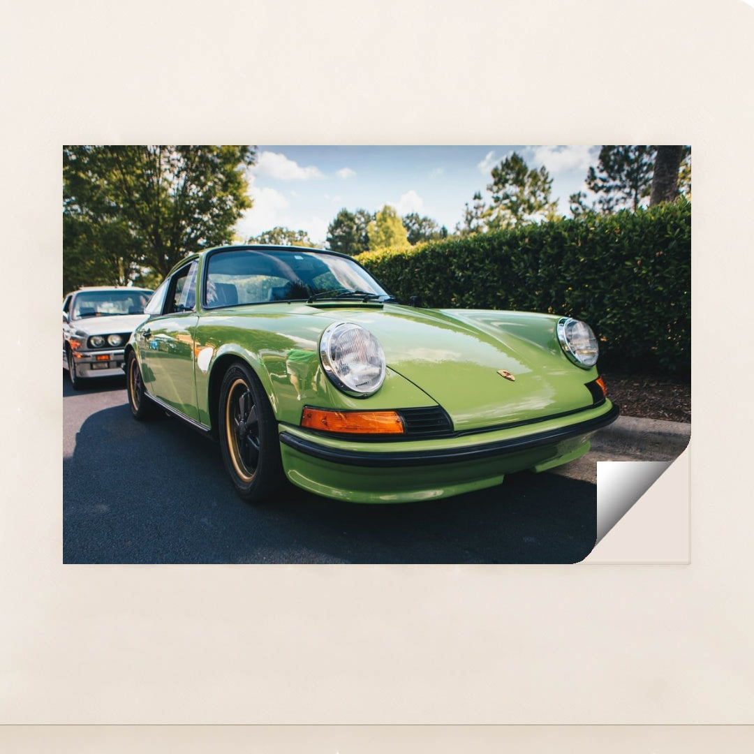 This photo shows a classic Porsche 911 in light green parked on a sunny street with trees in the background, minimalist unframed style.