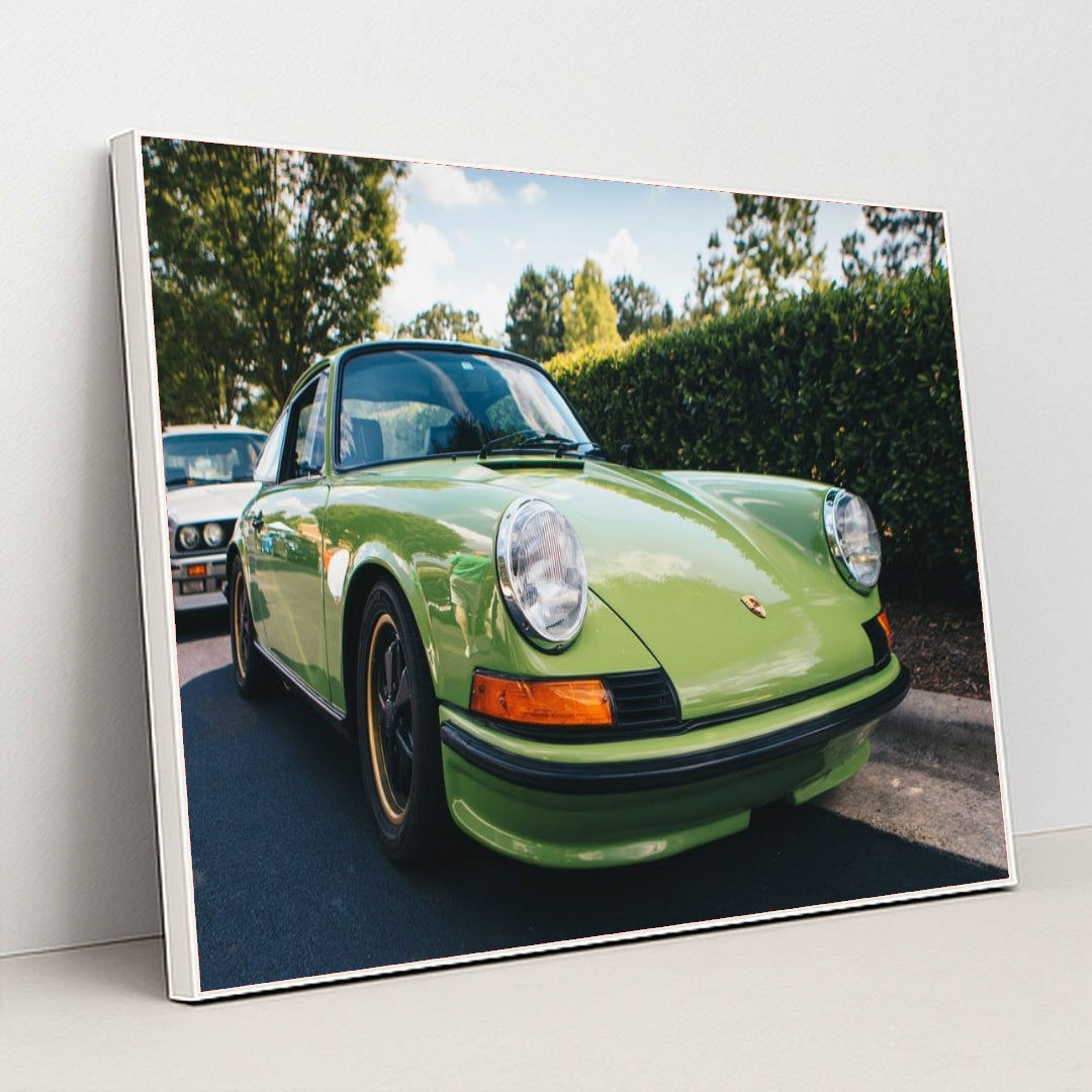 This photo shows a classic Porsche 911 in light green parked on a sunny street with trees in the background, in a white frame.