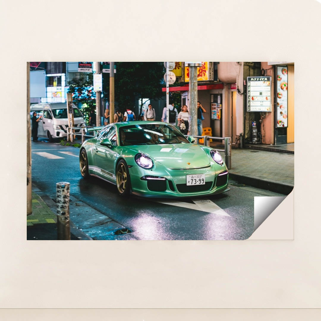 This photo shows a mint green Porsche sports car with gold wheels driving through a vibrant city street at night, minimalist unframed style.