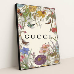 This artwork shows a floral Gucci design with colorful wildflowers, butterflies, and the Gucci logo on a pale background, in a black frame.