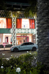 City of Indulgence nighttime wall art featuring a BMW sedan parked in front of an illuminated Gucci storefront.