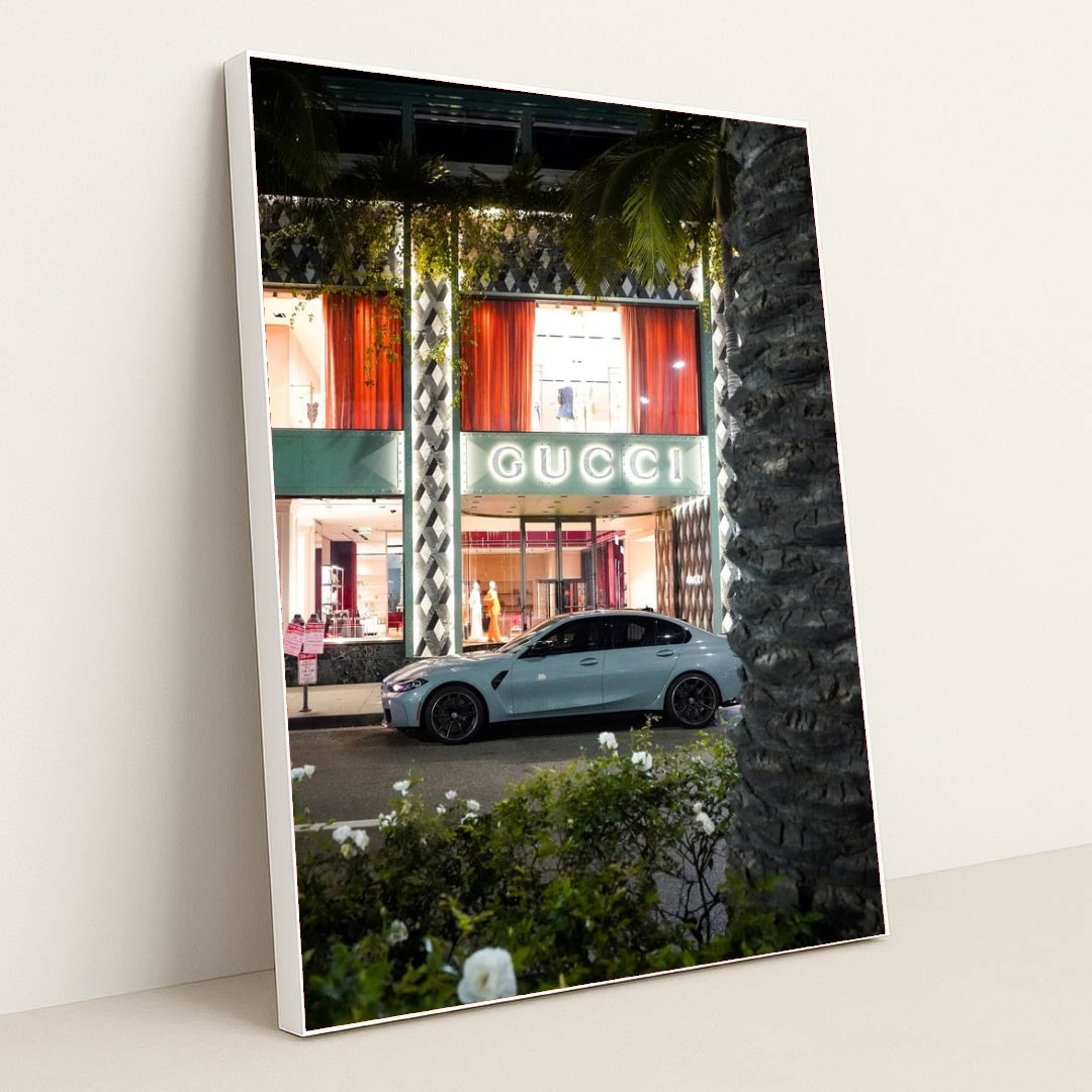 This photo shows a white BMW sedan parked in front of an illuminated Gucci store at night, in a white frame.
