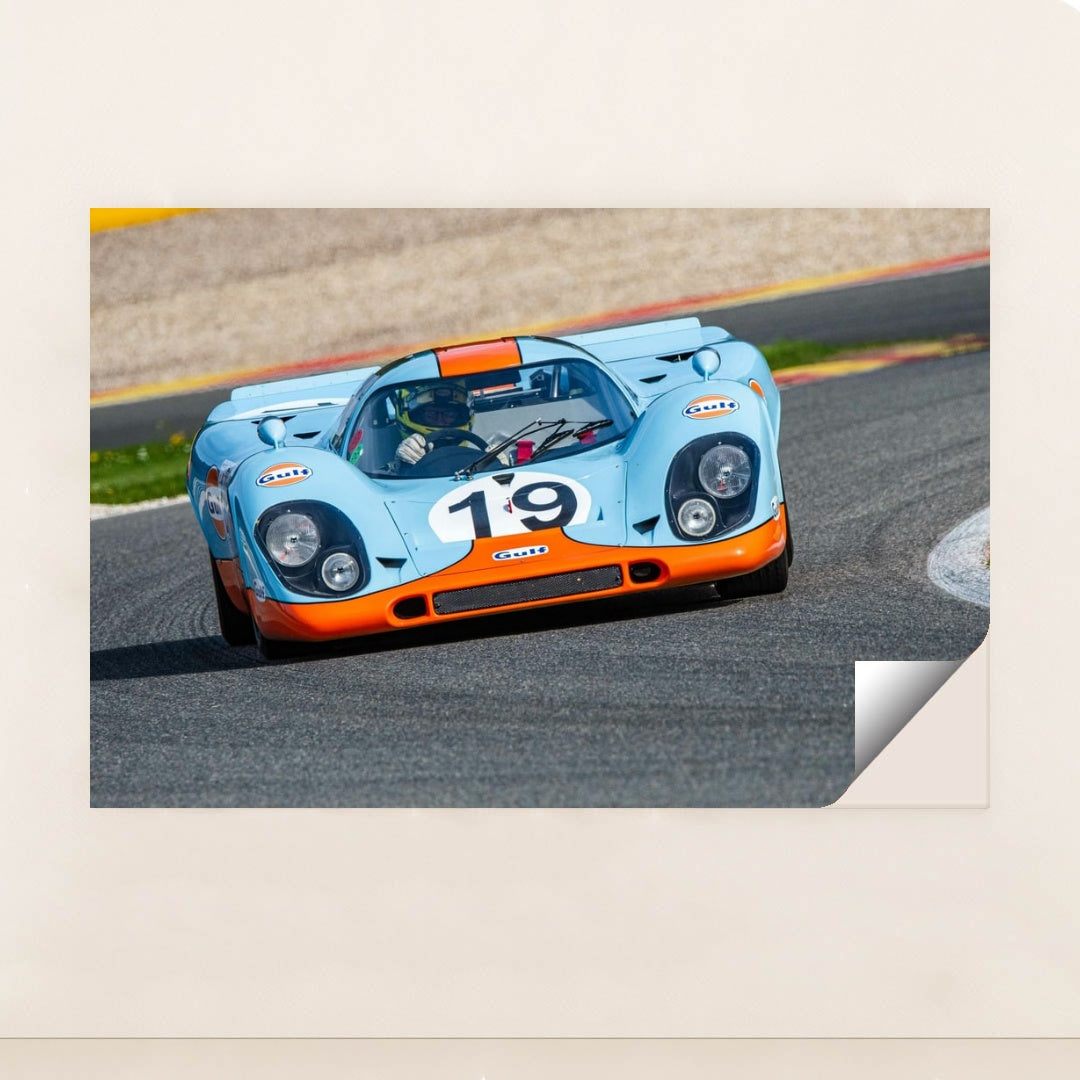 This photo shows a vintage blue and orange Porsche race car with the number 19 rounding a track corner, unframed.