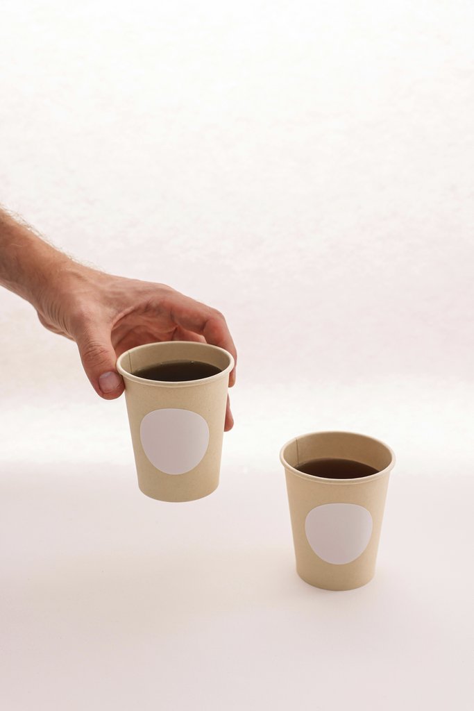 Cup of  Couple - A minimalist photo of two disposable coffee cups, one held by a hand, against a plain background.