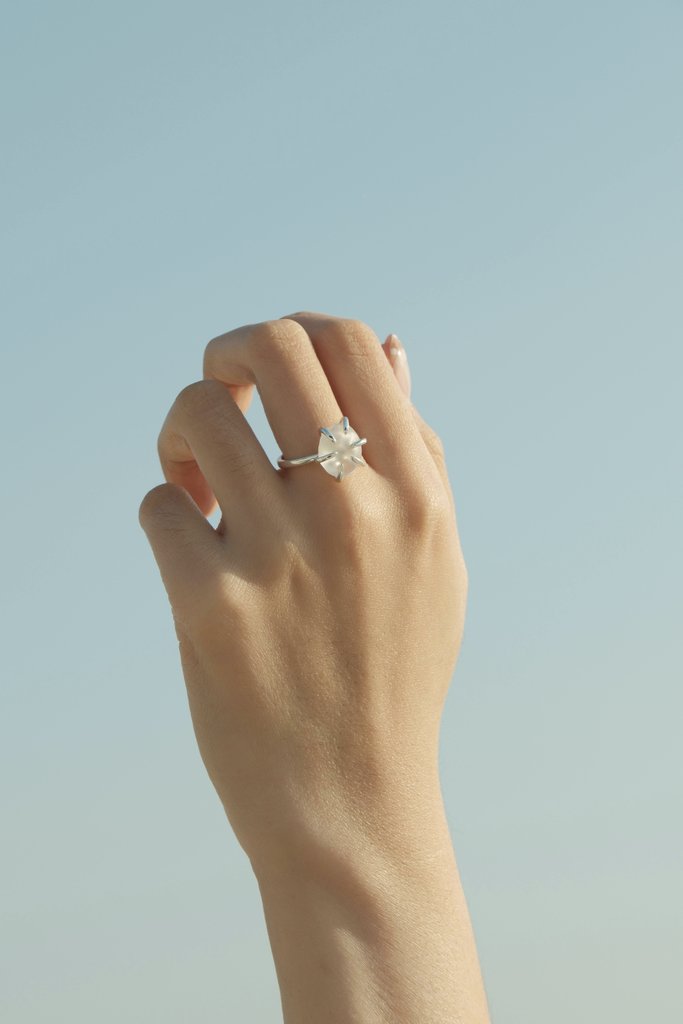 hana mori - A close-up of a hand wearing a diamond ring against a clear blue sky, showcasing elegance and simplicity.