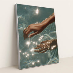 This artwork features a hand with rings reaching into sparkling blue water, in a silver frame.