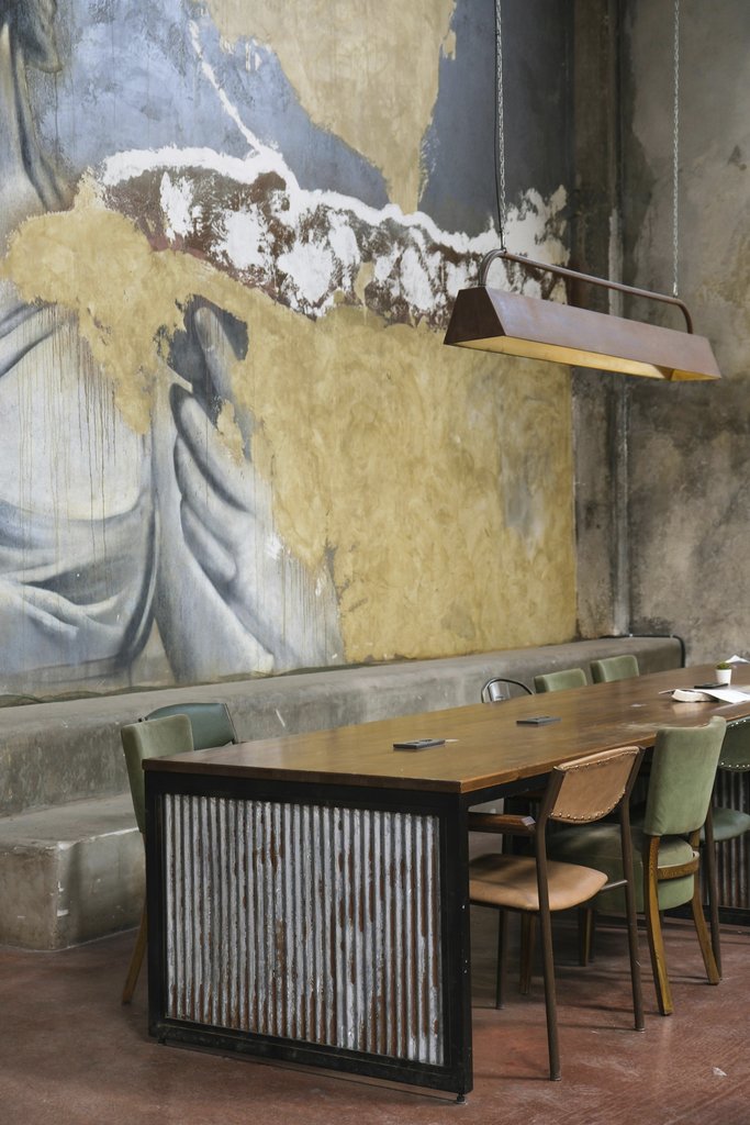 Merve Nur Türker - Industrial dining setup with mural wall art in a rustic atmosphere.