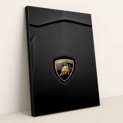 This photo shows a close-up of a Lamborghini badge on a matte black car hood, in a black frame.
