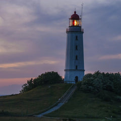 Illuminated Coastal Lighthouse on Hill During Evening Twilight by Karl Knips