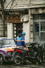 Unknown - A candid street view of a person in winter attire next to a colorful car and scooter in Istanbul.