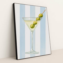This artwork features a classic martini glass with three green olives against vertical blue and white stripes, in a black frame.