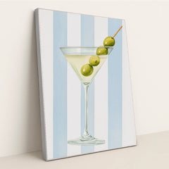 This artwork features a classic martini glass with three green olives against vertical blue and white stripes, in a silver frame.