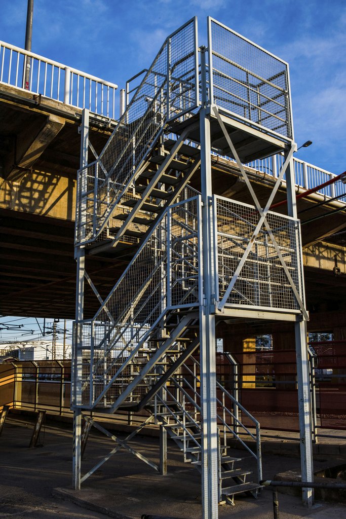 Victor  Moragriega - Dynamic urban scene featuring a sturdy metal staircase under an overpass.