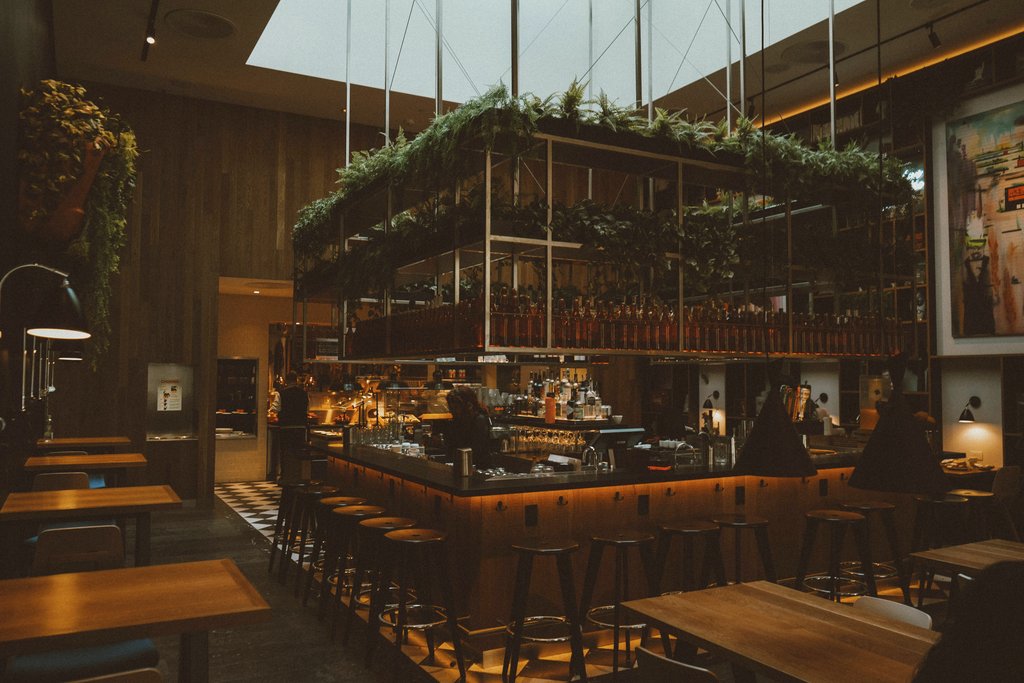 Shots by  Sandhu - Stylish indoor bar with modern decor, wooden finishes, and lush greenery in Los Angeles restaurant.