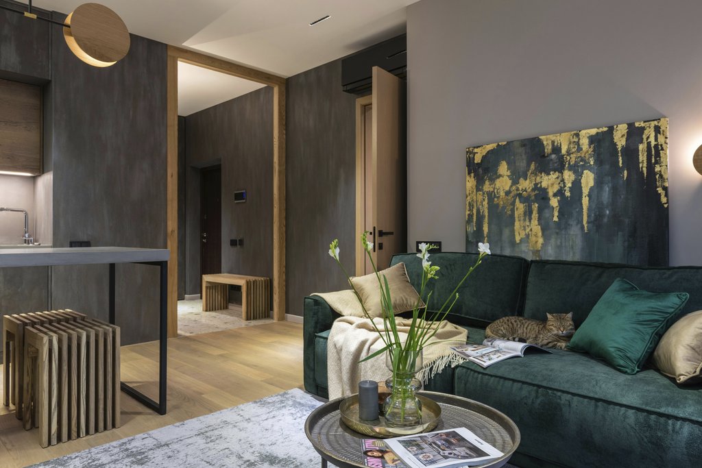 Max Vakhtbovycn - Stylish living room featuring a green velvet sofa, abstract art, and a cat lounging comfortably.