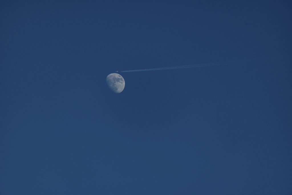 Diego F. Parra - A jet leaves a contrail near a waxing gibbous moon under a bright blue sky, highlighting aviation and astronomy.
