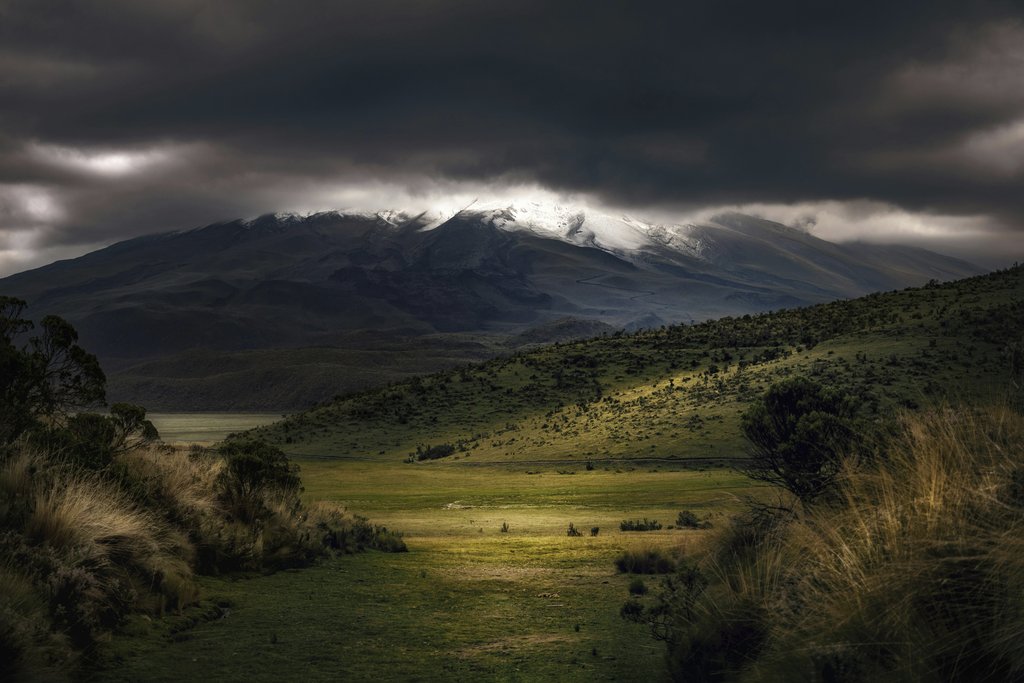 Simon Berger - Stunning mountain landscape with dramatic dark clouds and green terrain.