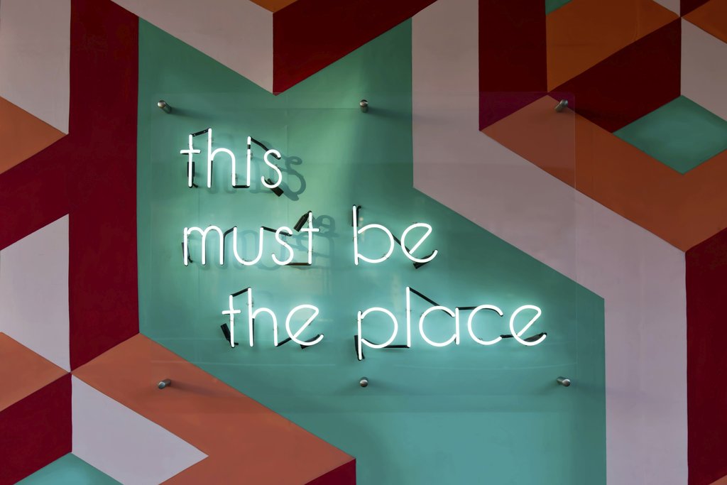 Tim Mossholder - Colorful geometric wall featuring a glowing neon sign with an inspirational quote.