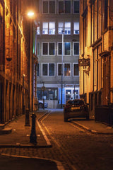 Michał Robak - A dimly lit urban alleyway at night with parked car and glowing streetlights, showcasing city atmosphere.