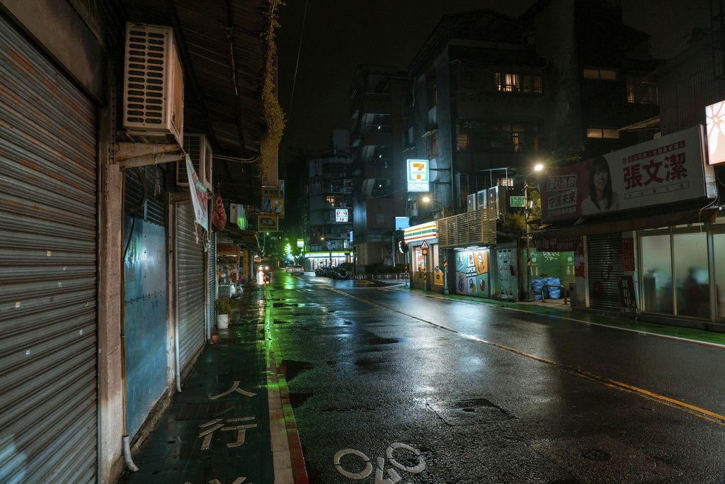 Jimmy Liao - A wet city street illuminated by neon lights at night, creating a moody urban atmosphere.