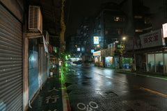 Jimmy Liao - A wet city street illuminated by neon lights at night, creating a moody urban atmosphere.