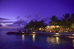 Asad Photo Maldives - A breathtaking view of a tropical resort at twilight, surrounded by palm trees and reflecting on the ocean.