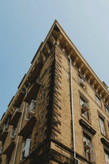 Keith Lobo - Low angle view of a weathered building facade with air conditioners set against a clear blue sky.
