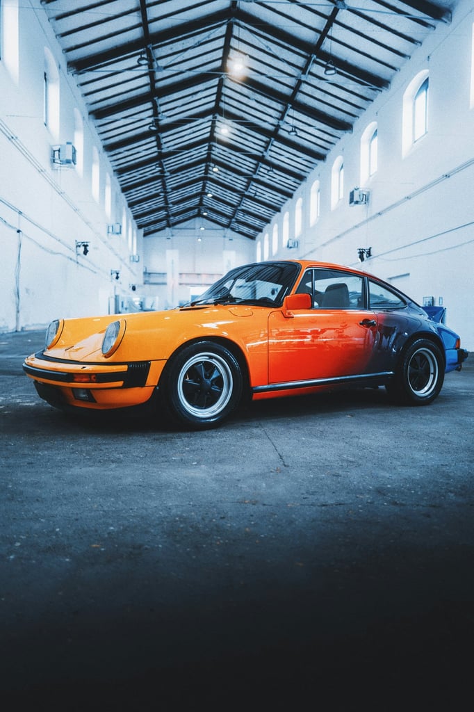 Classic Porsche 911 with Sunset Fade parked in an industrial space, showcasing vibrant orange-to-blue gradient paint and polished wheels.