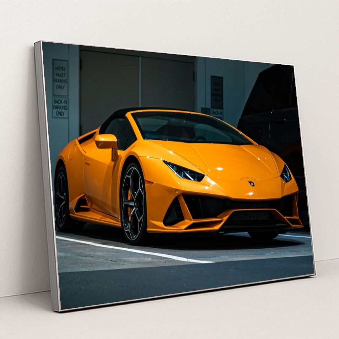 This photo shows an orange Lamborghini Huracán Spyder parked in a valet area at night, in a silver frame.