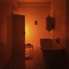 Camille Bonneau - Dimly lit bathroom with red hue, open door, bathtub, and chair in Lyon, France.