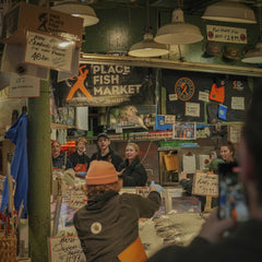 Eddie Ortiz - Lively atmosphere of Pike Place Fish Market with people engaged in fish tossing and sales activities.