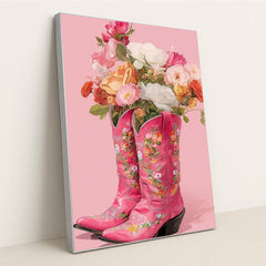 This artwork shows two pink floral cowboy boots filled with colorful roses and flowers against a solid pink background, in a silver frame.