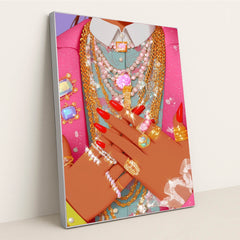 This artwork shows hands with red nails adorned with multiple sparkling gold and silver rings and necklaces over a pink jacket, in a silver frame.