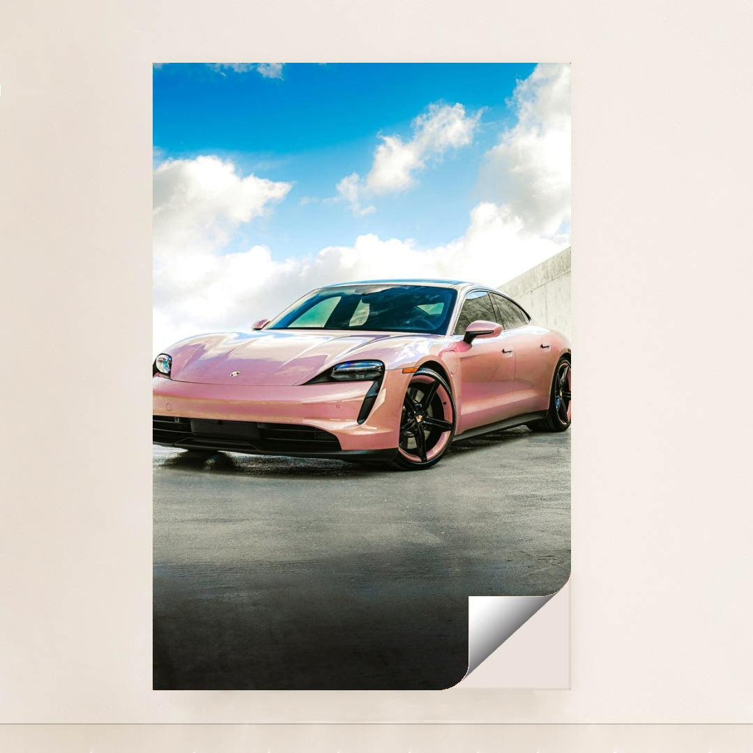 This photo shows a pink Porsche Taycan electric sports car parked outside under a blue sky with clouds, minimalist unframed style.