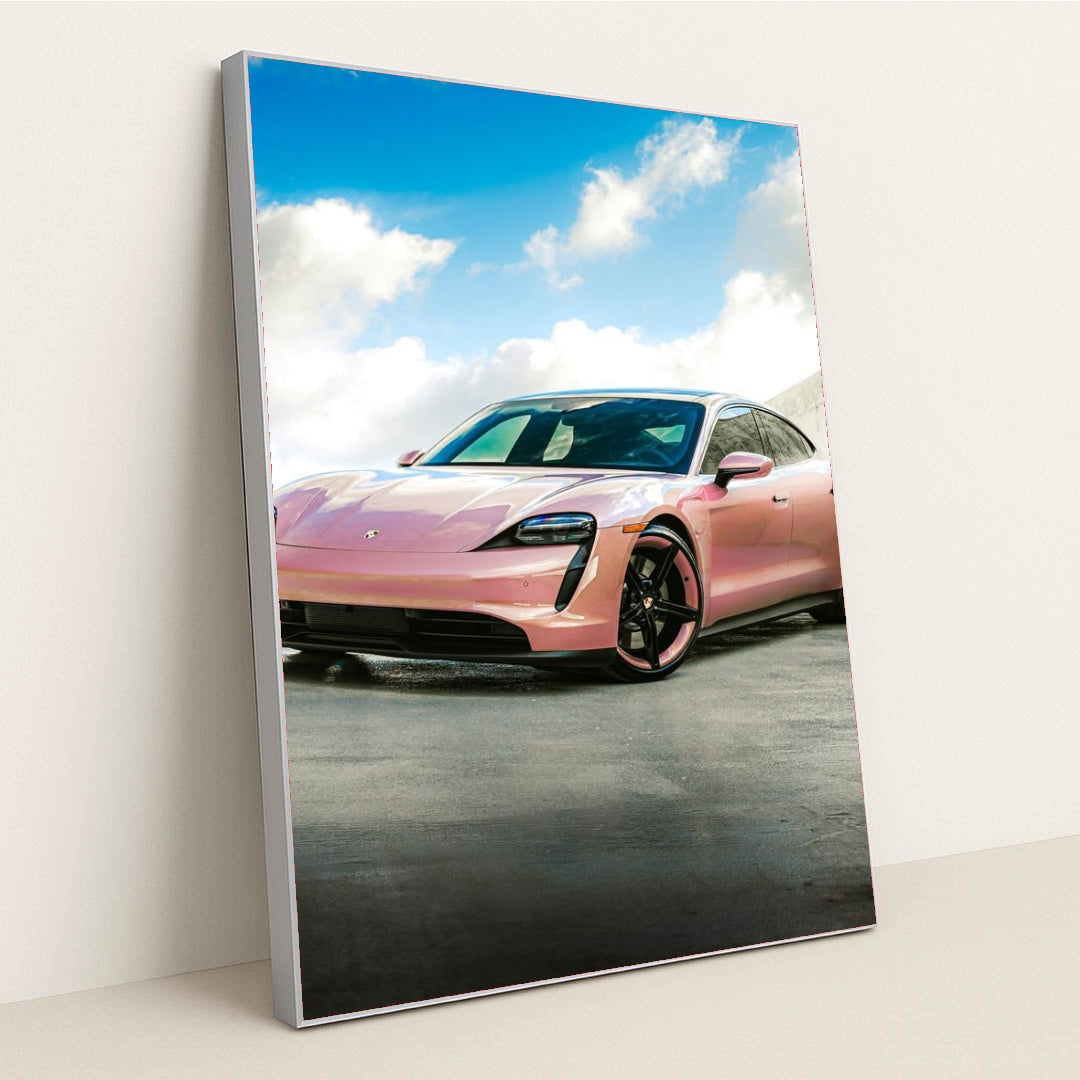 This photo shows a pink Porsche Taycan electric sports car parked outside under a blue sky with clouds, in a silver frame.
