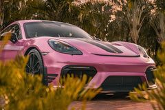 Porsche Spyder Framed by Foliage, metallic pink sports car with black stripe, amidst tropical palms at sunset.