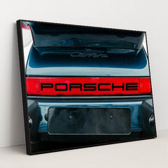 This photo shows the rear of a classic Porsche Carrera with a bold red Porsche logo and open trunk, in a black frame.