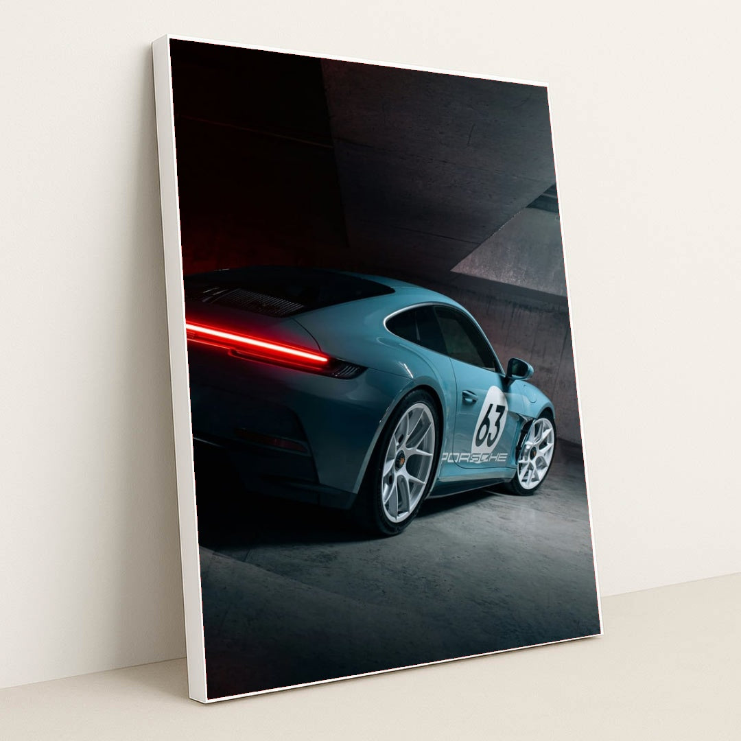 This photo shows a silver Porsche sports car with number 63 and glowing taillights in a modern concrete garage, in a white frame.