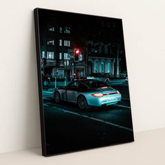 This photo shows a silver Porsche 911 coupe waiting at a red traffic light on a city street at night, in a black frame.