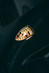 Close-up of the Porsche Emblem in Focus on a black hood, showcasing its gold and crimson details as car wall art.