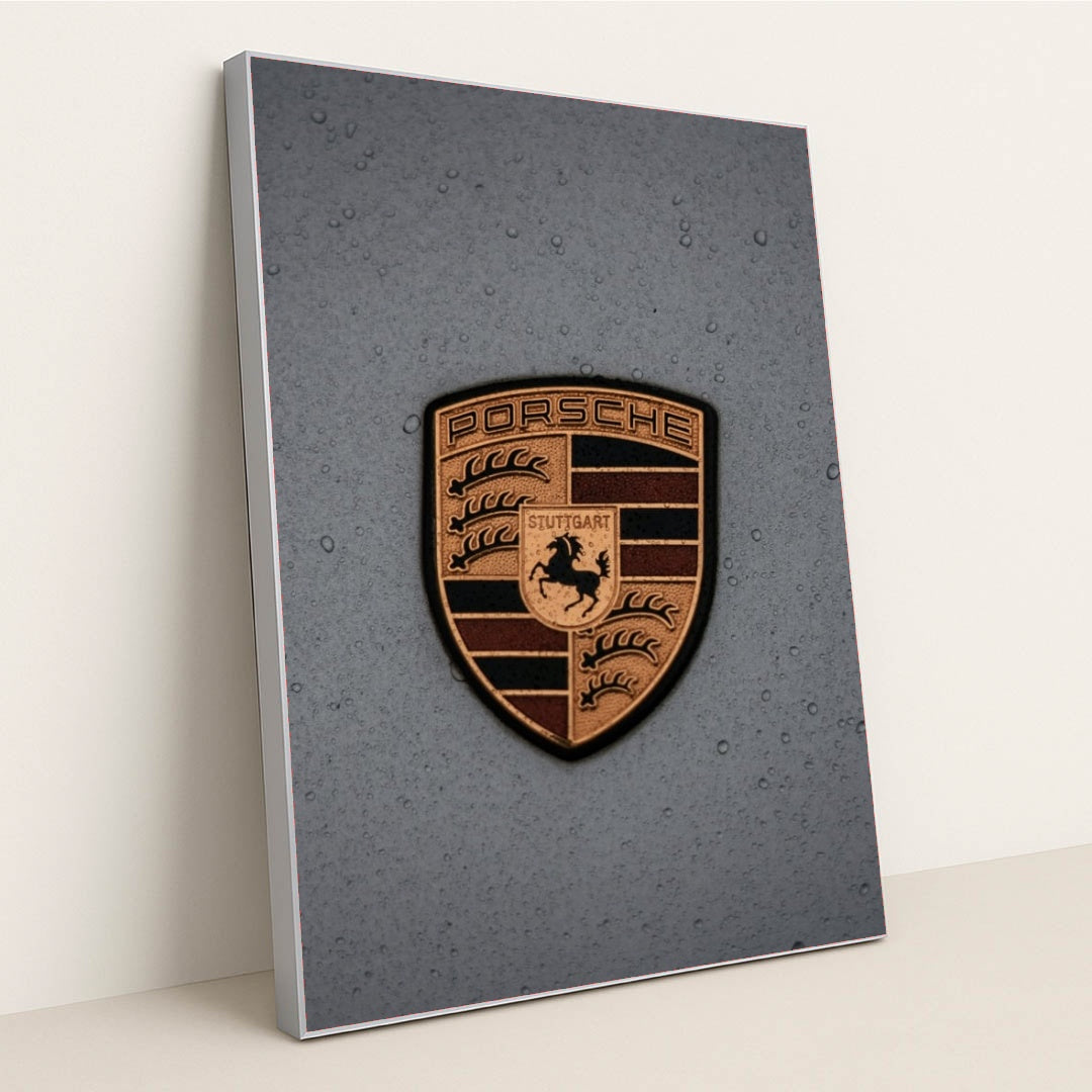 This photo features a gold Porsche emblem with raindrops on a gray car hood, in a silver frame.