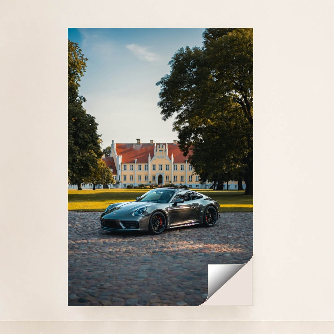 This photo shows a silver Porsche sports car parked on a cobblestone driveway in front of a large historic mansion, unframed.